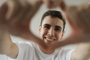 https://www.pexels.com/photo/young-man-smiling-and-making-a-heart-shape-with-his-hands-9775451/ Young man with short black hair smiling