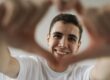 https://www.pexels.com/photo/young-man-smiling-and-making-a-heart-shape-with-his-hands-9775451/ Young man with short black hair smiling